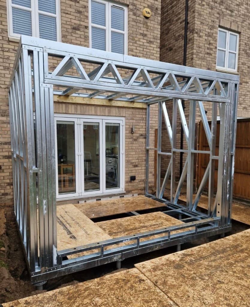 L-shaped steel frame home extension raised on screw piles in a garden